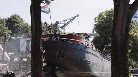 an old moored houseboat flying the dutch flag with steamy smoke on a summery day