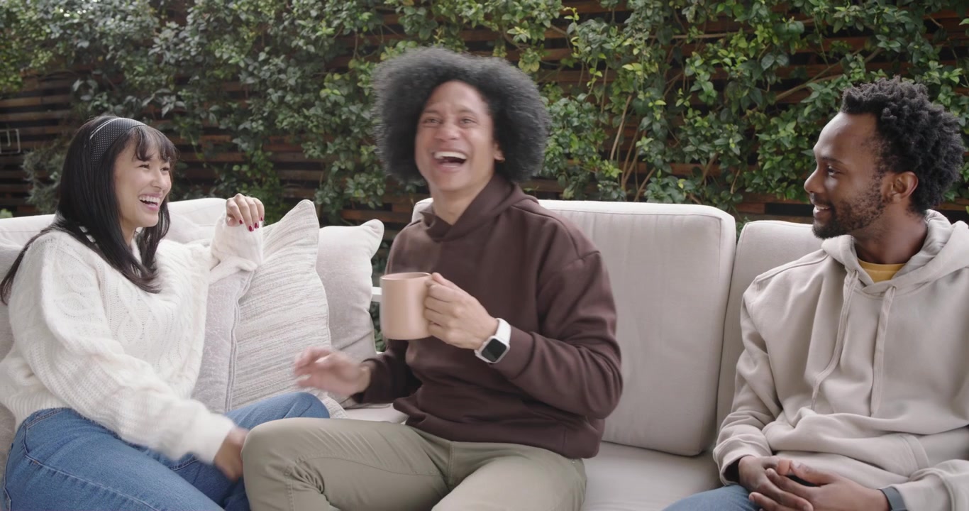 Diverse group patio sofa center man reaching hand causing laughs turning to include man holding mug