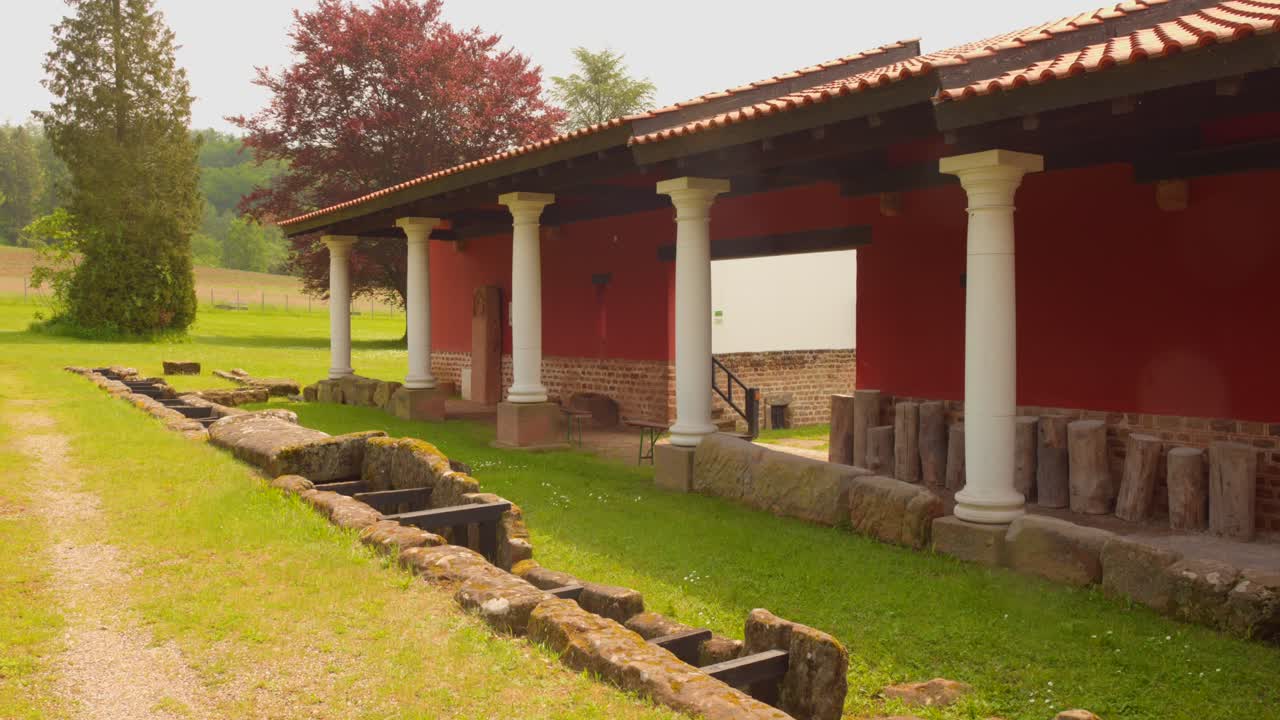 Ancient Roman building with red walls and white columns in a grassy outdoor museum setting