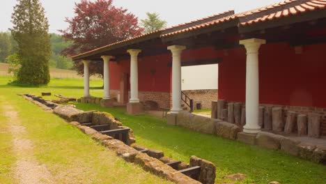 ancient roman building with red walls and white columns in a grassy outdoor museum setting