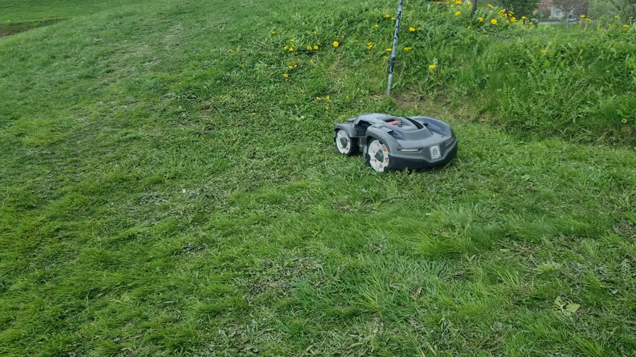 A robotic lawn mower moves in all directions across a green lawn at Kristiansten Fortress in Trondheim, Norway, demonstrating technology taking over human tasks
