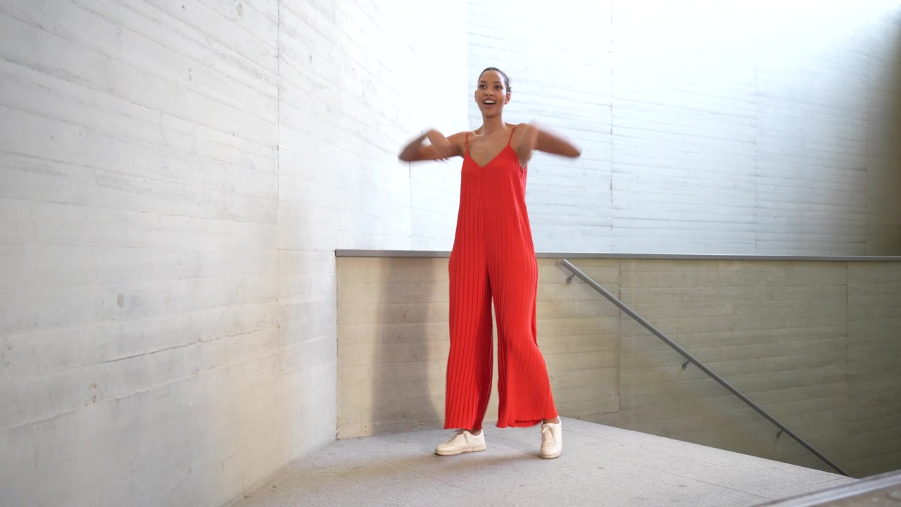 A fashion model dressed in a striking red jumpsuit is performing in a minimalist space