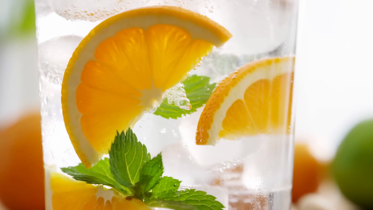 Close Up Glass With Orange Slices And Mint Leaves In Sparkling Water, Ice Cubes And Bubbles Rising,