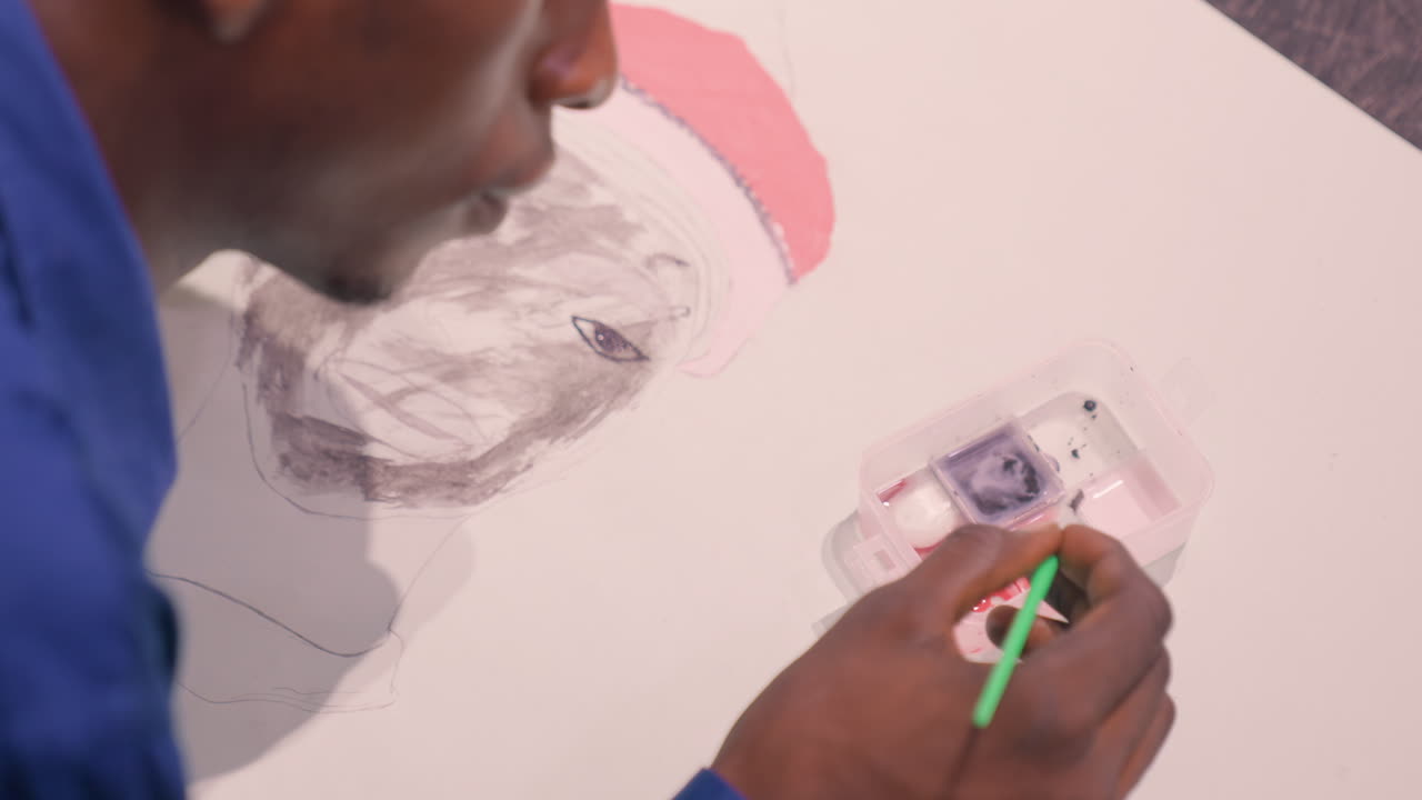 Black man painting portrait with palette, illustrator mixing colors on plastic tray, green brush strokes, blue shirt, pink beanie sketch, closeup of hand refining facial features, calm creative