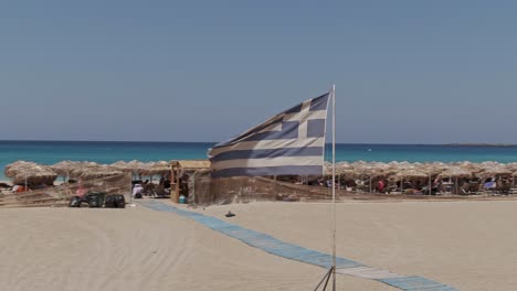 wawing greece flag in resort of falasarna beach in crete island, drone orbit view