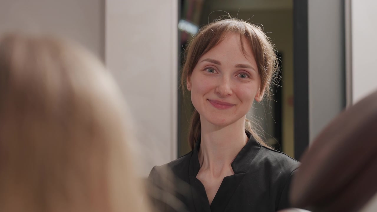Primo piano di una donna in abbigliamento professionale che conversa con un'altra donna, probabilmente discutendo di servizi dentali o ortodontici. La scena presenta un'illuminazione soffusa e dettagli di un ambiente interno.