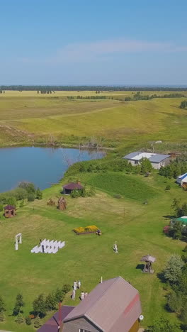 wedding venue with arch and seats on green field at calm lake under boundless blue sky on warm autumn day aerial view