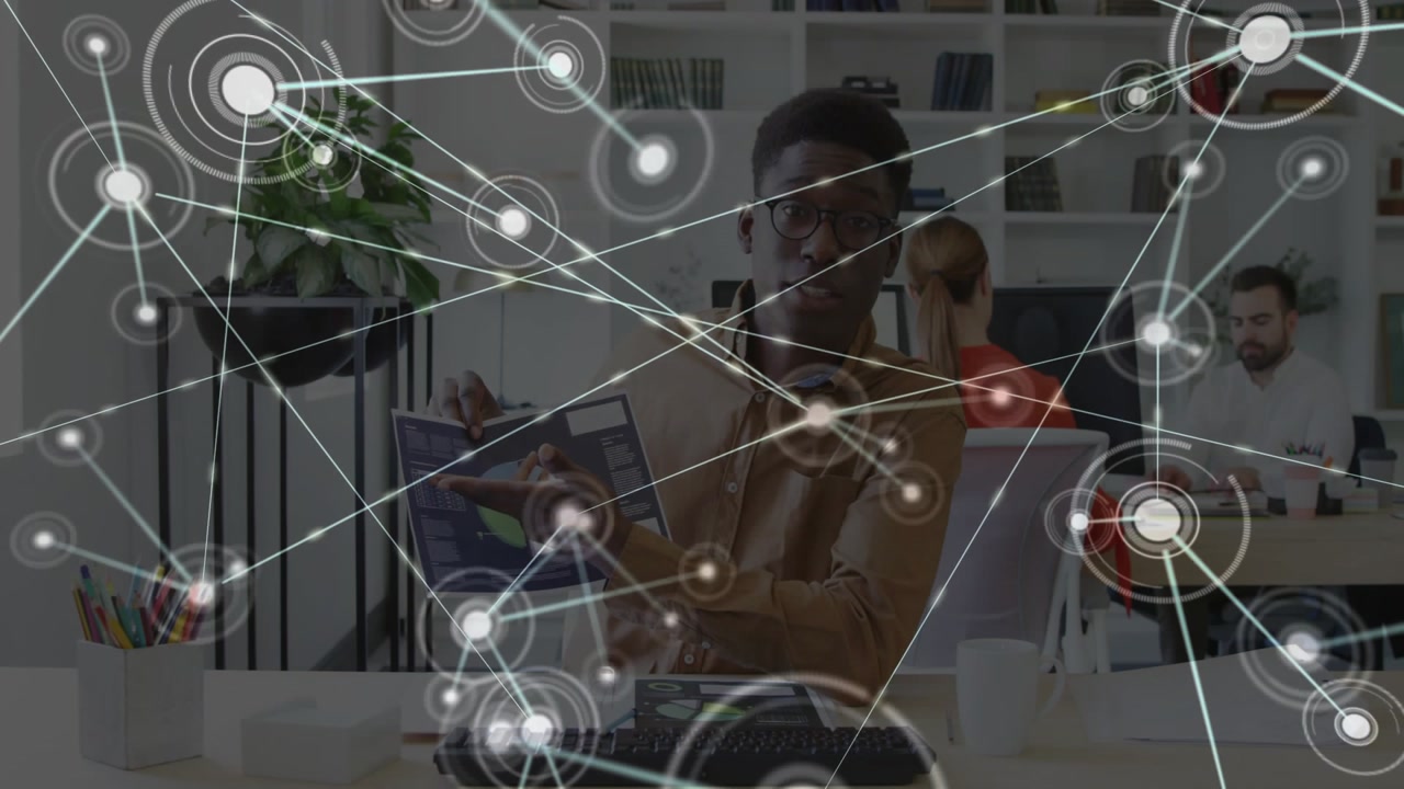 Network overlay appearing, man sitting at desk gesturing, picking tablet displaying analytics