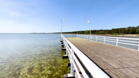 Muelle-De-Madera-Que-Se-Extiende-Hacia-El-Tranquilo-Mar-Azul-Bajo-Un-Cielo-Despejado-En-Jurata,-Polonia