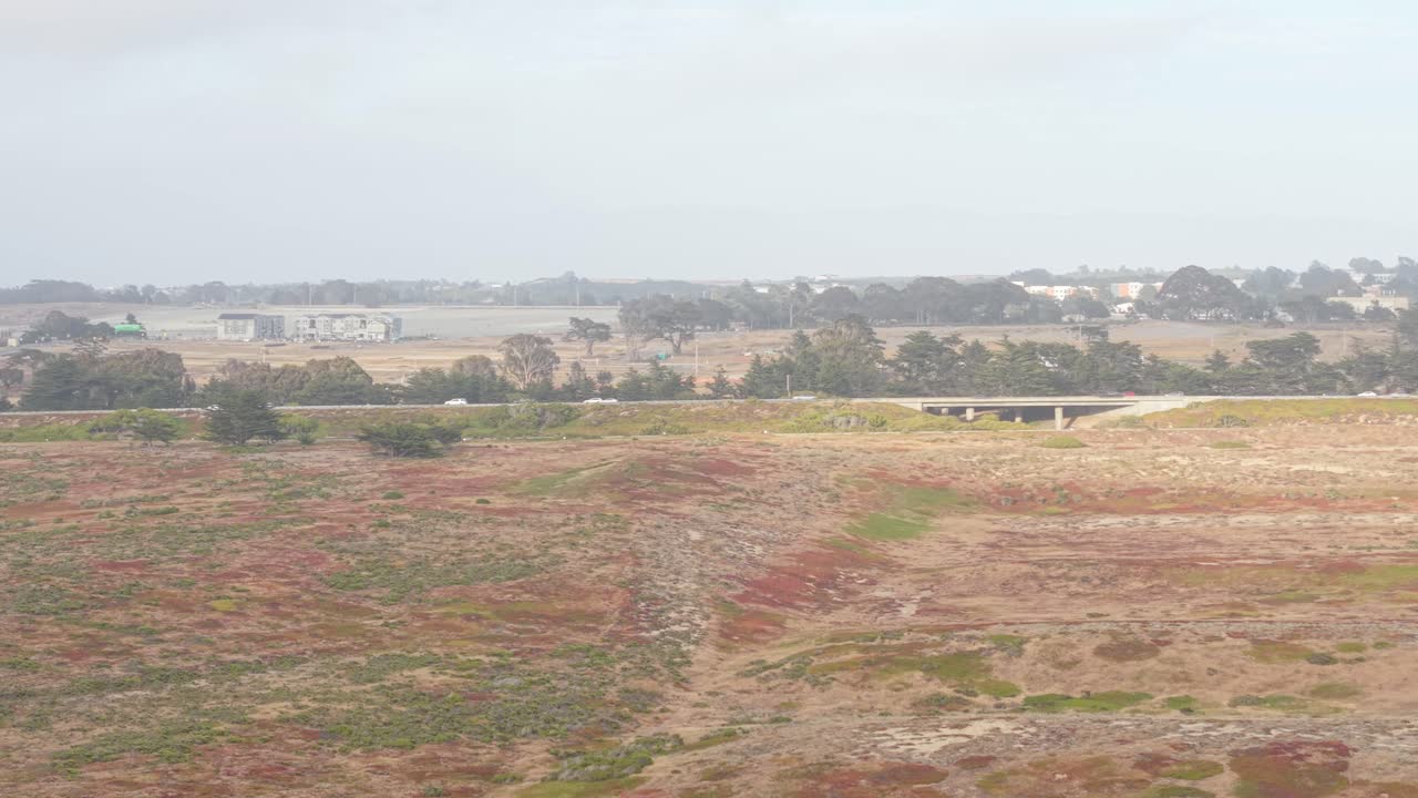 Open skies and rugged terrain surround Fort Ord, with a faint glimpse of cars rolling along Highway 1.