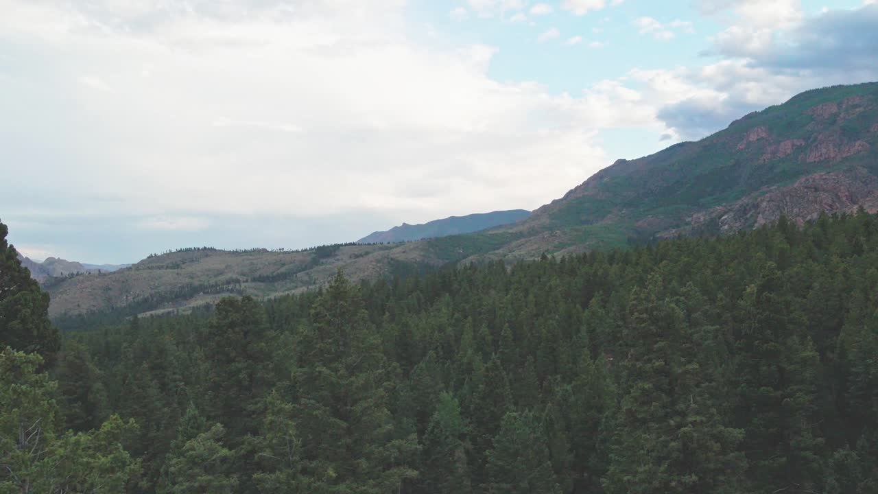 A slow drone flight revealing a remote mountain forest at sunset with wilderness area and rocky cliffs in the distance. Filmed in the Pike National Forest of Colorado