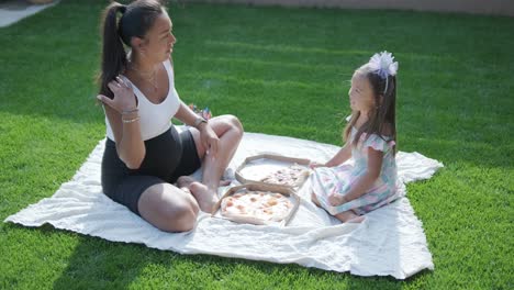 una madre e hija disfrutan de un picnic de verano al aire libre en un césped cubierto de hierba, compartiendo pizza y pasando tiempo de calidad juntos en un día soleado. la escena de unión familiar refleja ocio y relajación.