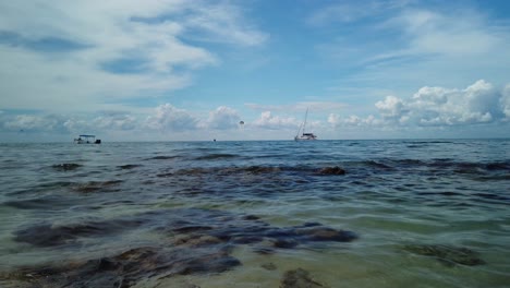 Stunning-warm-clear-water-surrounding-Cozumel,-Mexico-with-boats-on-the-horizon-and-a-beautiful-blue-tropical-sky