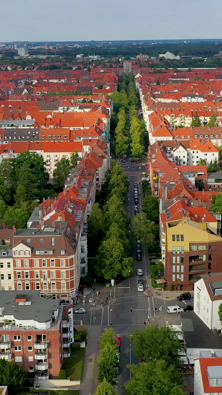 Ripresa verticale cinematografica con drone di una strada alberata ad Hannover, Germania, con architettura classica dai tetti rossi e verde urbano