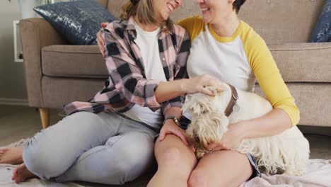 caucasian lesbian couple smiling while playing with their dog at home