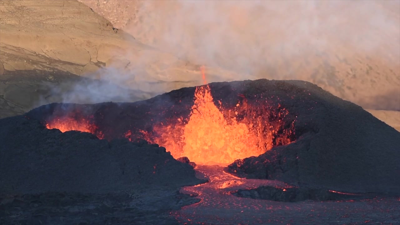Vista aerea con drone di un'eruzione vulcanica attiva in Islanda che mostra lava fusa brillante che scorre da una bocca vulcanica attraverso un campo di lava di basalto scuro con vapore che sale