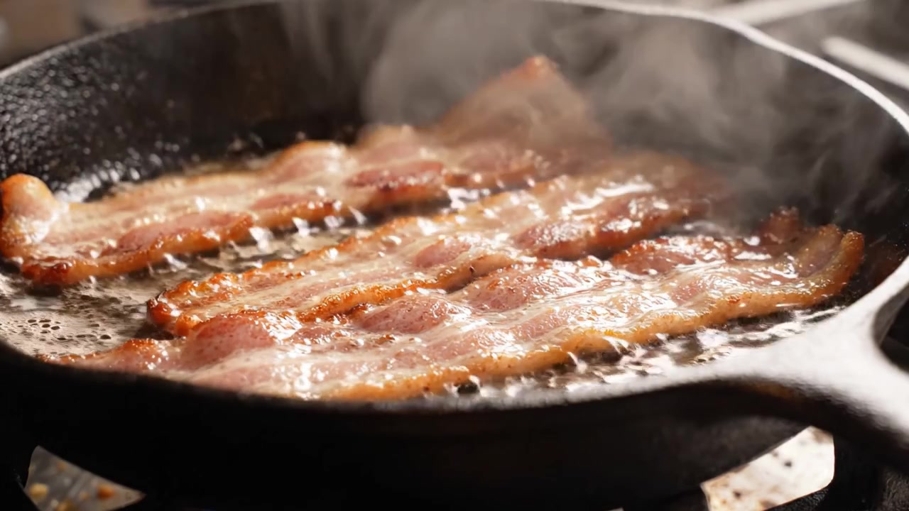 Pancetta sfrigolante che cuoce in una padella di ghisa, catturando l'aroma appetitoso e la croccantezza dorata di un classico della colazione.