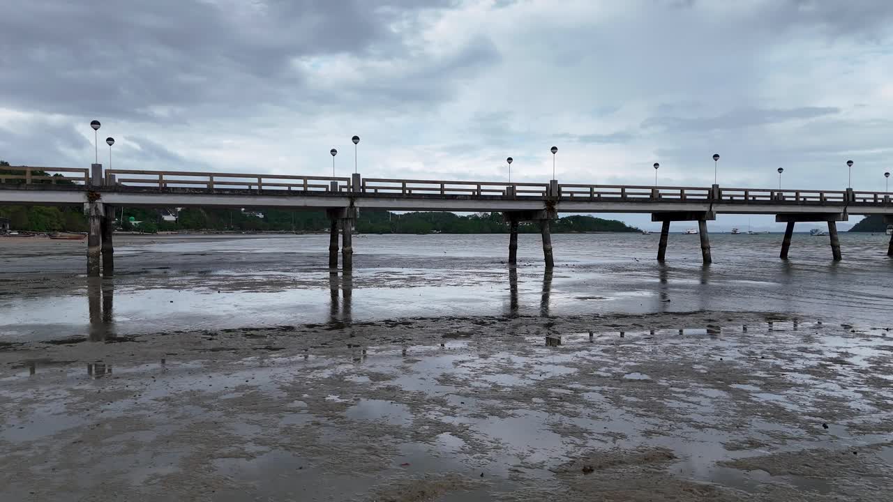 Aerial footage captures a serene fishing pier in Phuket, Thailand, under overcast skies, highlighting the tranquil coastal environment