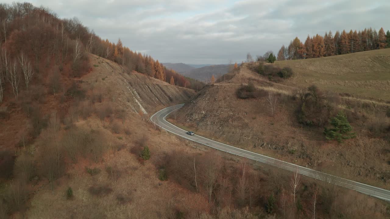 una vista aérea de un dron de un coche conduciendo por una carretera sinuosa que atraviesa un cañón a finales de otoño