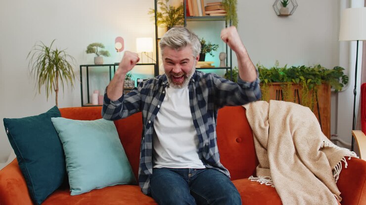 Happy Caucasian senior man watching TV shouting celebrating success winning goal achievement