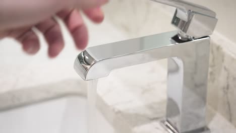 a person reaches into frame and turns on the stylish silver faucet in slow motion