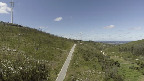 Wind-Turbines-Rotating-On-The-Green-Mountains-In-Reguengo-Do-Fetal,-Batalha,-Portugal-On-A-Sunny-Day---wide-angle,-ascending-drone-shot