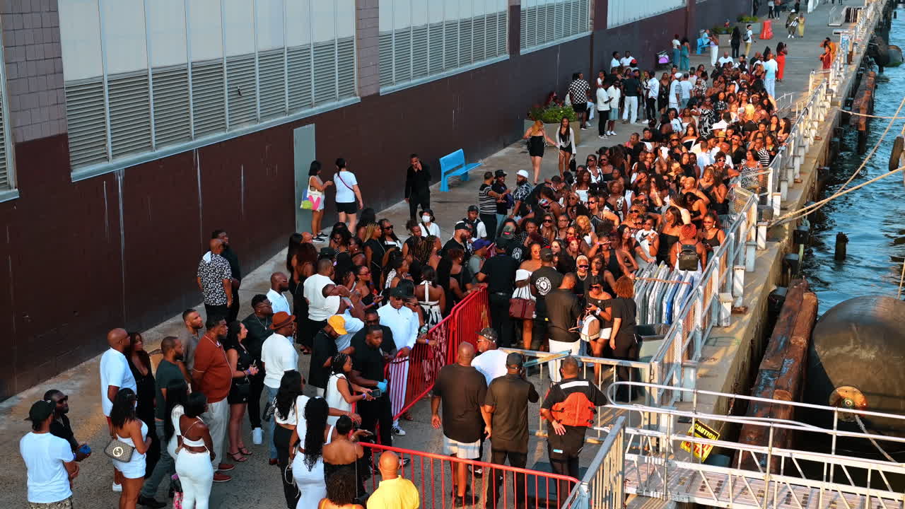 New York, USA, 5 agosto 2025: Grande folla di persone in attesa all'ingresso del molo del porto. Gruppo eterogeneo di persone in fila su una banchina di cemento vicino a un fiume nel tardo pomeriggio.