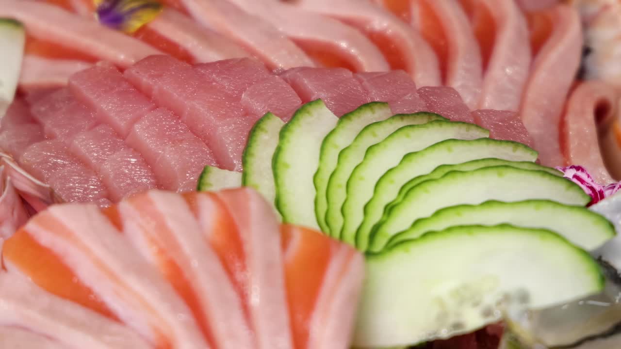 A detailed view of sliced tuna and salmon with cucumber and shrimp garnishes.
