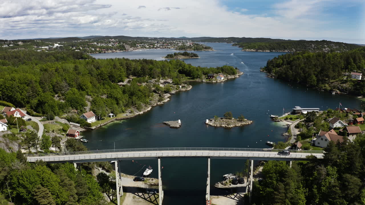 Aerial Drone shot of cars driving over Justøy Bridge in Lillesand, Norway. Fjords can be seen continuing into the distance as boats travel along them.
