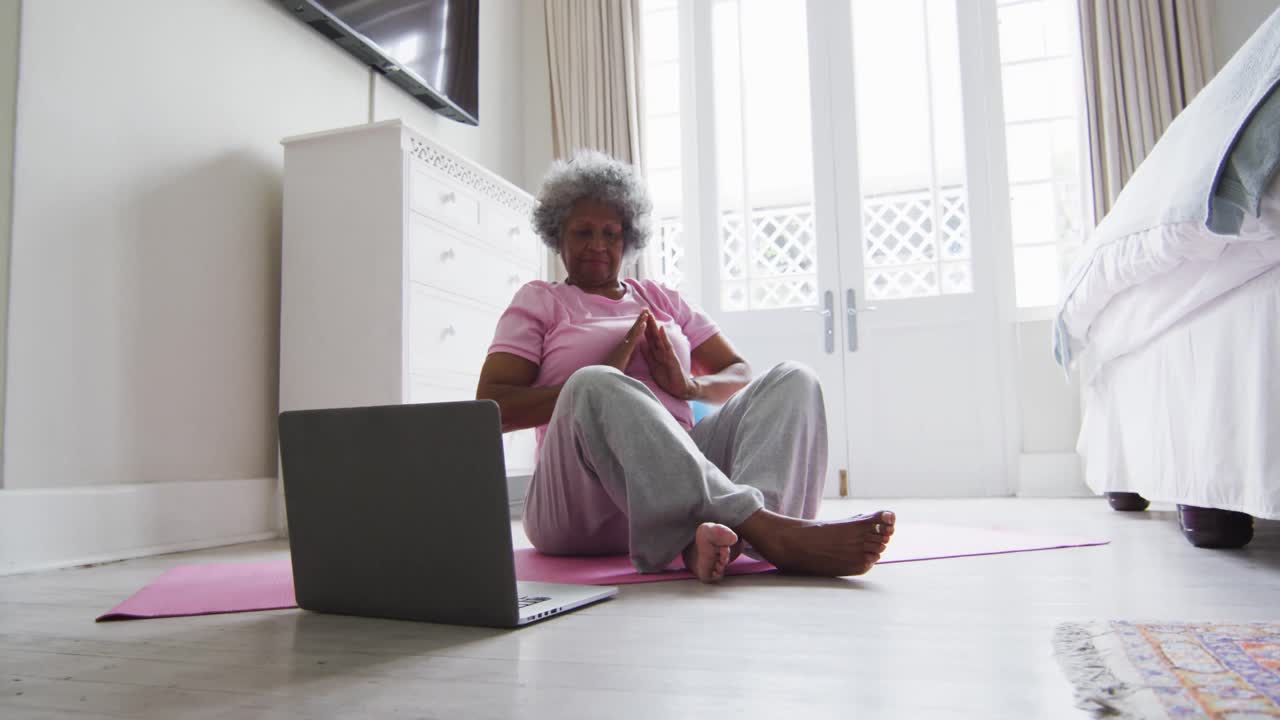 Senior african american woman practicing yoga while looking at laptop at home