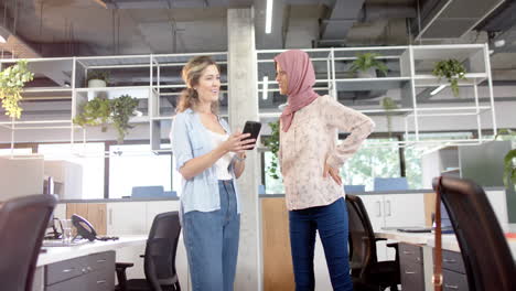 happy diverse creative female colleagues in discussion using smartphone in office, slow motion