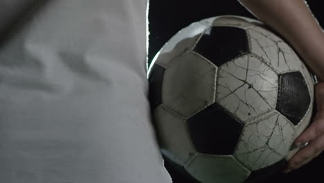 camera focuses soccer ball held by boy illuminated by a spotlight at night