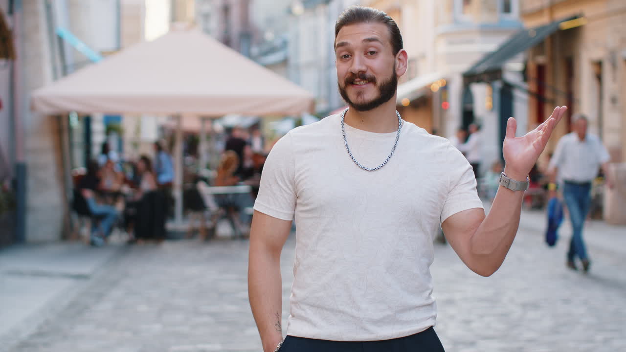 joven sonriendo amistosamente a la cámara agitando las manos hola hola saludo o adiós en la calle de la ciudad