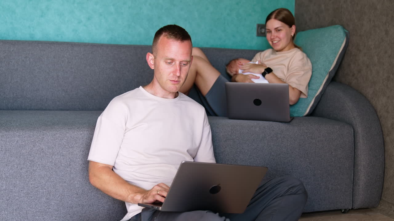 Happy parents of a newborn baby working remote from office. Mom and dad work on their laptops at home and nursing a child.