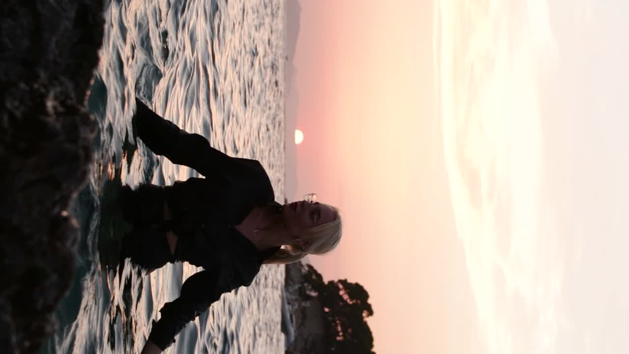 atractiva chica rubia en el mar adriático, con una camisa negra con gafas, salpicaduras y poses en el agua durante la puesta de sol en dubrovnik, croacia