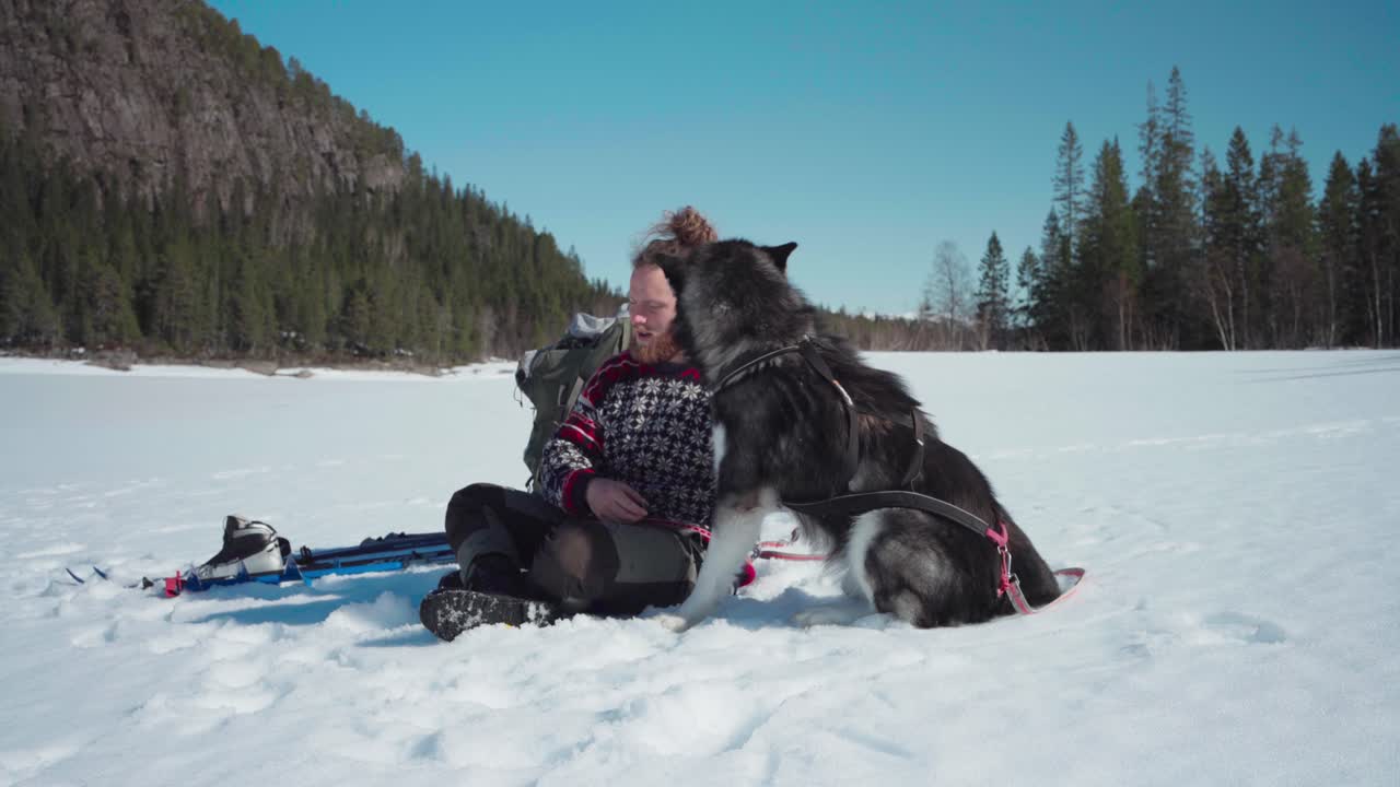 Norweg przytulający swojego psa rasy Alaskan Malamute w zimowej, zamarzniętej scenerii.
