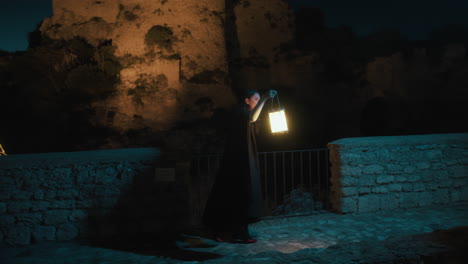 mysterious woman with cloak and lantern walks near a vintage castle