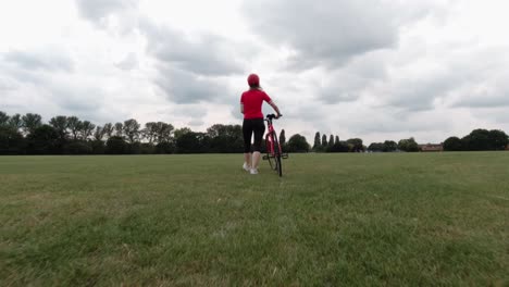 Kaukasische-Radfahrerin-Im-Roten-Oberteil,-Die-Mit-Ihrem-Fahrrad-In-Einem-Park-In-Zeitlupe-Geht