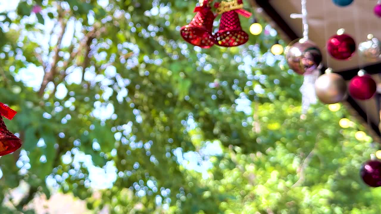 Red bells and colorful ornaments hang against a backdrop of lush green leaves, creating a vibrant outdoor scene.
