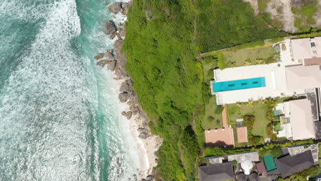 Top-down-overhead-aerial-view-of-Bali-coastline-with-luxury-tropical-villas-on-the-cliff-and-sand-beaches-with-turquoise-blue-ocean-below