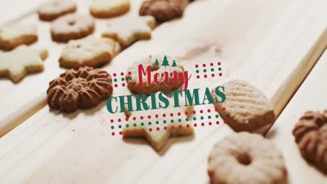 animation of merry christmas over cookies on wooden surface