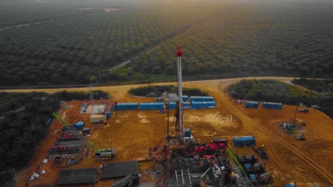 cinematic drone footage of onshore drilling rig equipment structure for oil exploration and exploitation in the middle of jungle surrounded by palm oil trees during sunset and high oil price