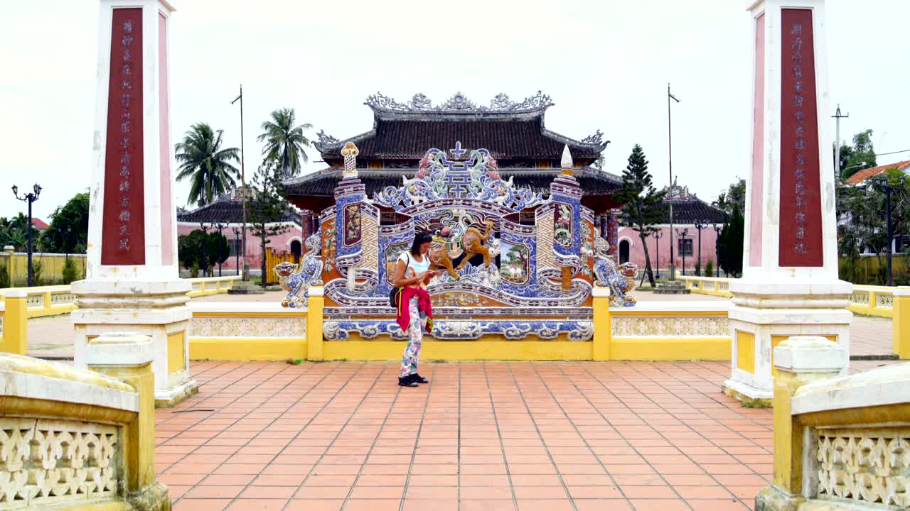 una mujer está de pie en un templo budista y usa un teléfono inteligente