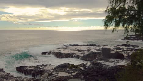 4k hawaii kauai pan left to right backlit ocean waves building left to right landing on small cove and crashing against rocky shoreline with mostly cloudy sky