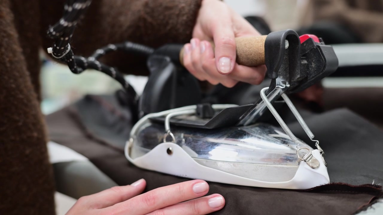 Close up of a tailor using a professional steam iron on black fabric in a fashion workshop