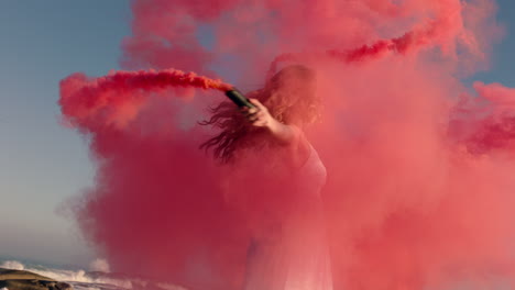 mujer bailando con una bomba de humo rosa en la playa al amanecer celebrando la libertad creativa con un giro de baile juguetón en cámara lenta