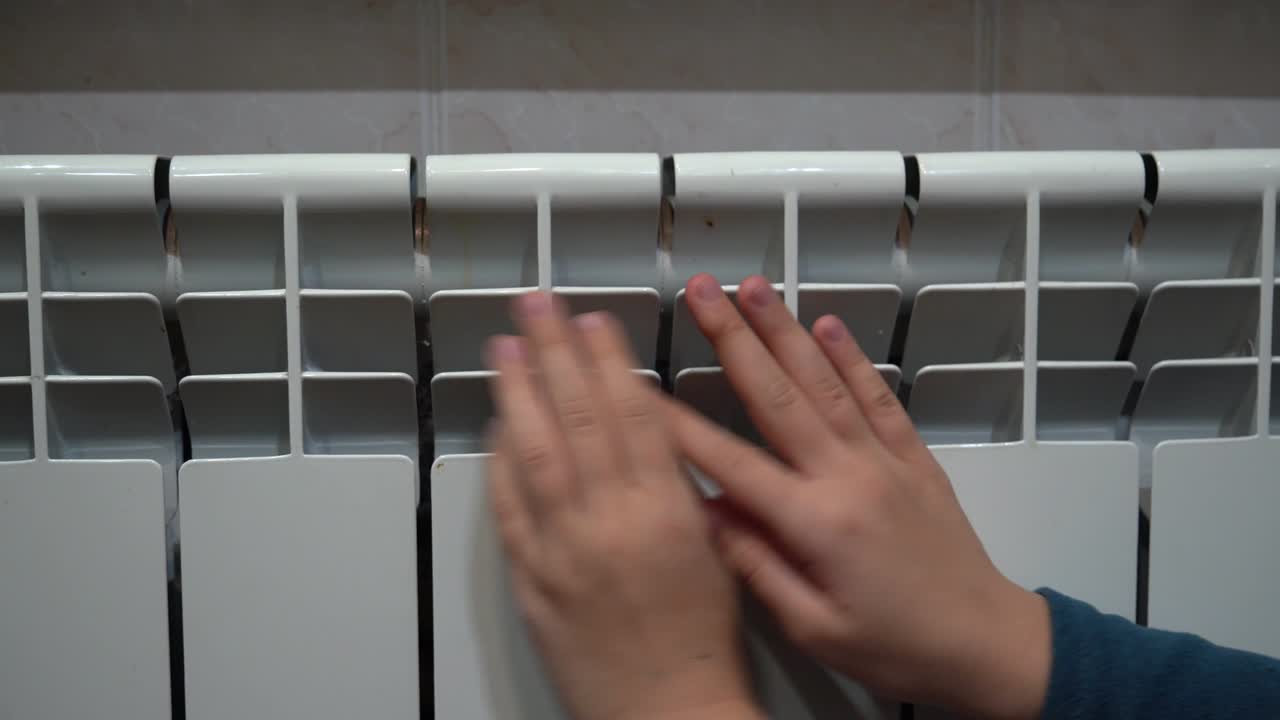 Children's hands warm up near a warm home radiator.