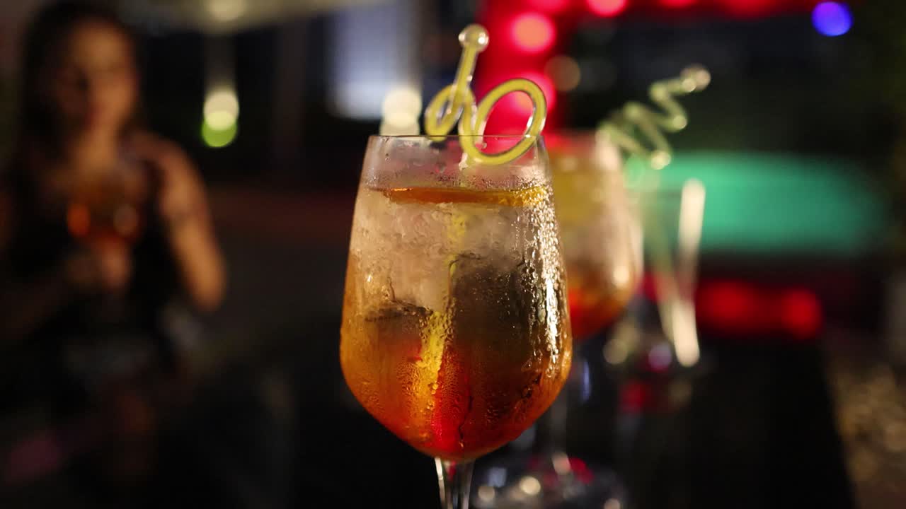 A woman enjoys a colorful cocktail in a dimly lit bar, creating a lively and inviting atmosphere