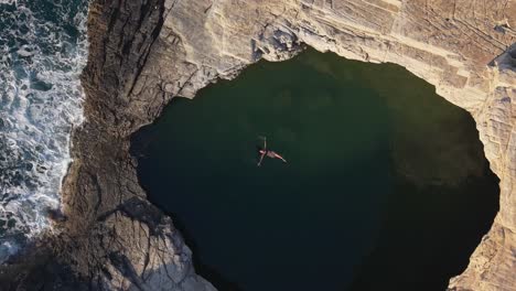 Aerial top-down footage of Giola in Thasos, capturing a woman swimming in the emerald natural pool surrounded by dramatic rocks and turquoise sea