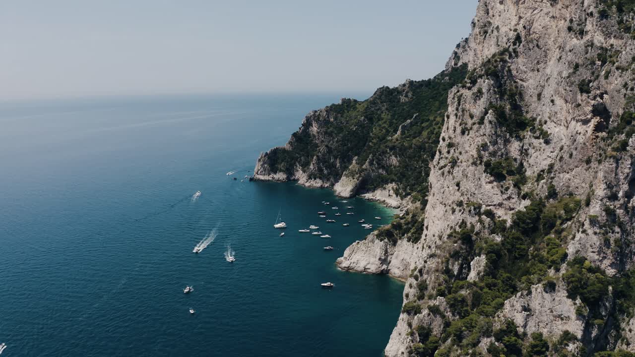 Drone shot of Capri, Italy's steep cliffs leading to boat-filled warm water